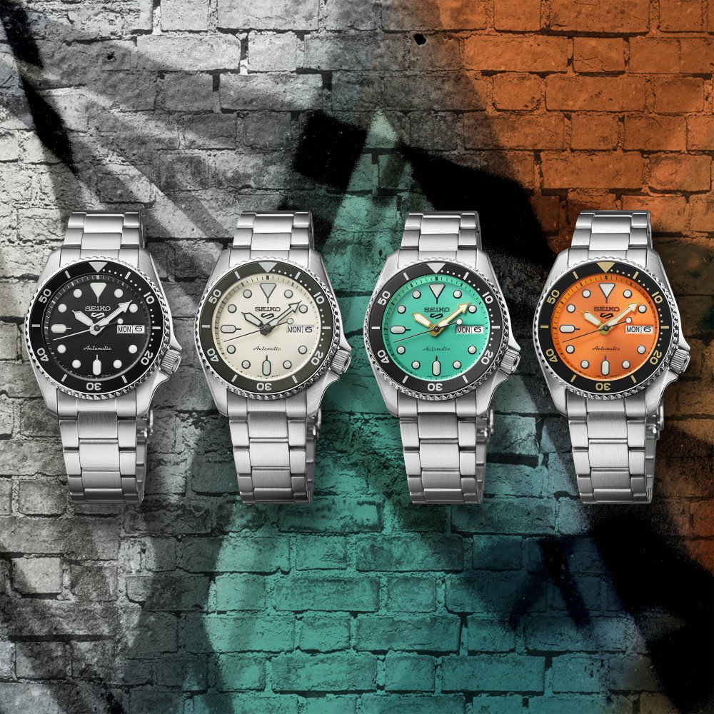 Histoire de Seiko, montre Seiko 5 Sports alignées sur un fond mural coloré, présentant plusieurs variations de cadrans et bracelets en acier pour illustrer l’univers dynamique et accessible de la marque japonaise.